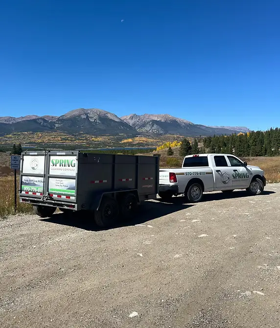 Spring Cleaning Company truck with trailer and junk in the back, mountain range and building in background - junk removal and hauling in Summit County Colorado